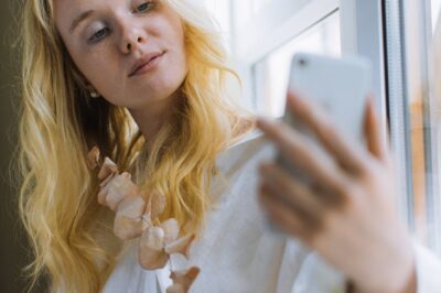 woman in white long sleeve shirt holding a smartphone